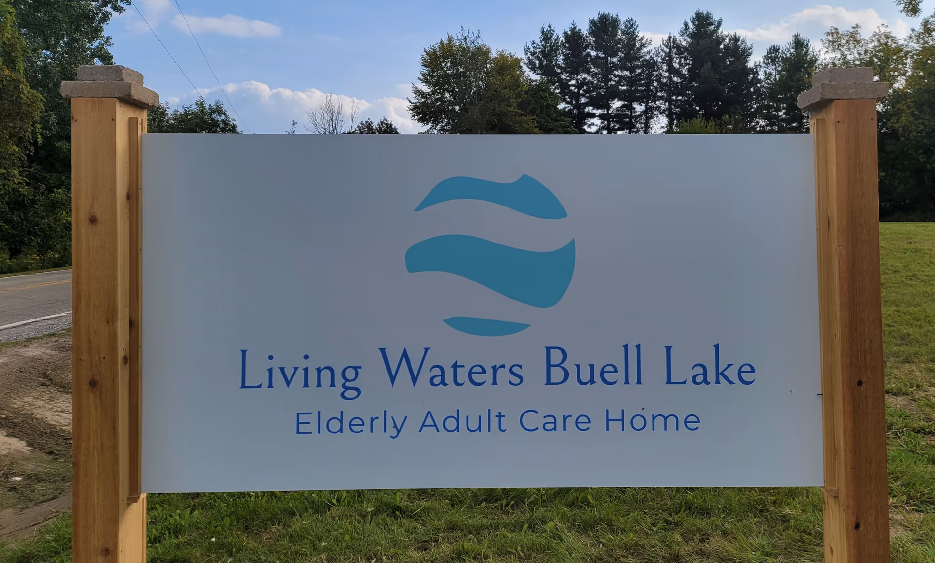 Large sign reading Living Waters Buell Lake with wooden posts beside a road