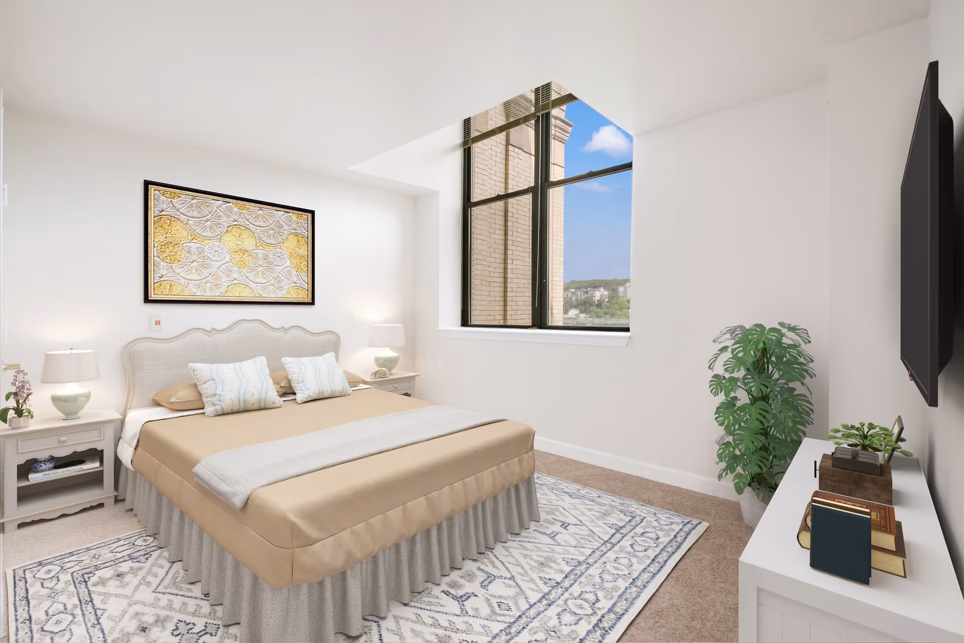 A bright bedroom with a large window showing a view of a brick building and blue sky. The room features a bed with beige bedding and two pillows, two bedside tables with lamps, a patterned rug, a white dresser with books and plants, and a wall-mounted TV.