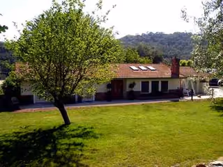 A single-story care facility with a red roof, green lawn, and trees in the yard.