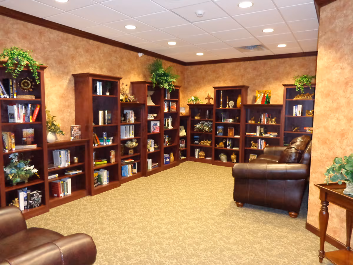A cozy reading lounge with multiple wooden bookshelves, decorative plants, and leather armchairs.