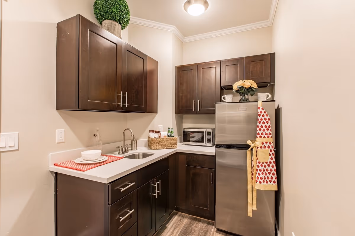 Small kitchenette with dark wood cabinets, a stainless steel mini-fridge and microwave, a sink and countertop accessories.