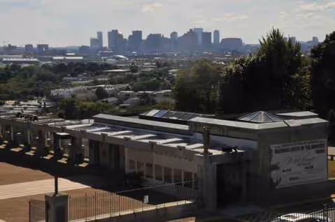 Exterior view of a facility with a walkway, fence, and distant city skyline.