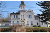 White, multi-story building with a turret, front steps, and surrounding trees.