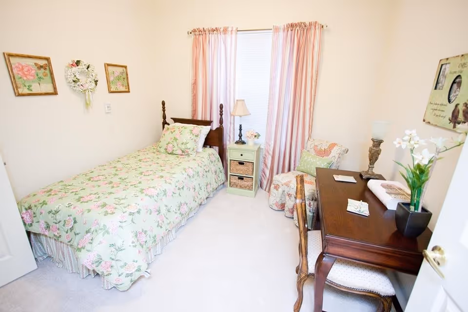 Small bedroom with a single floral bed, nightstand, desk, and chair.