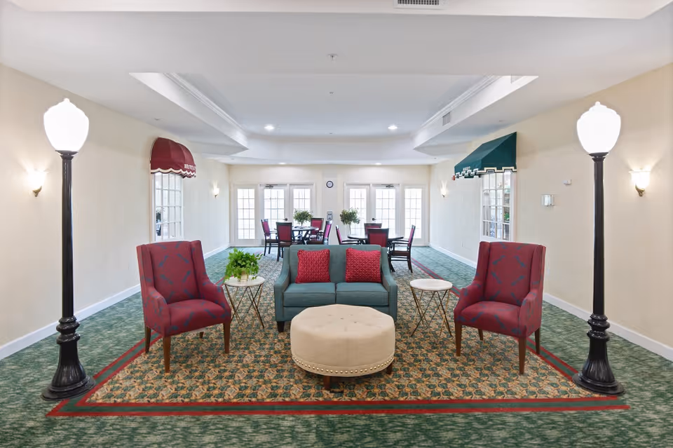 Communal lounge area with a sofa, two armchairs, an ottoman and side tables on patterned carpet, flanked by decorative streetlamp-style floor lamps.