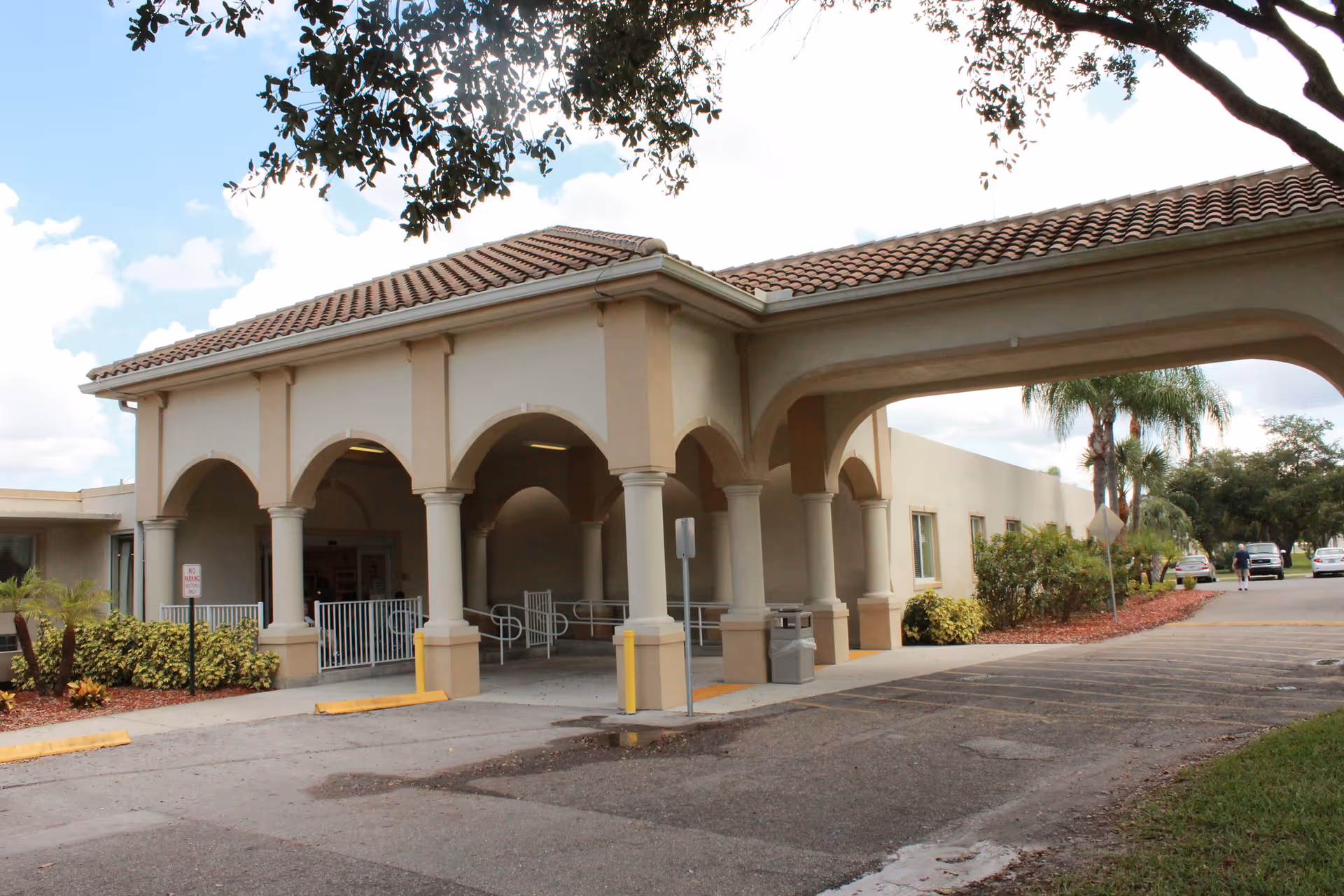 Front entrance of a health and rehabilitation building with an arched portico, columns, and a covered drop-off driveway.