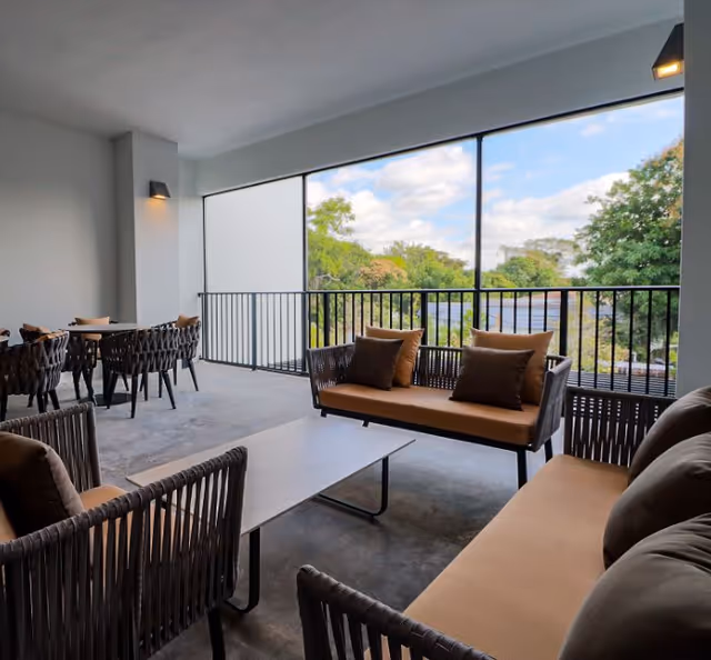 Covered balcony seating area with wicker sofas, a coffee table and dining chairs overlooking trees.