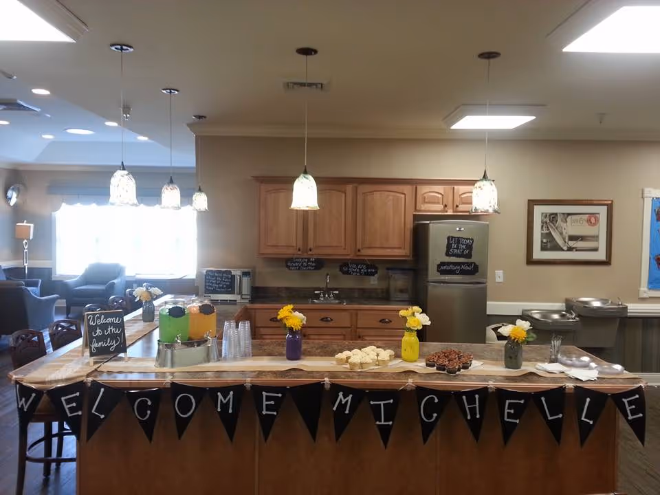 Decorated kitchen island in a senior living common area with a 'Welcome Michelle' banner, refreshments, and pendant lights.