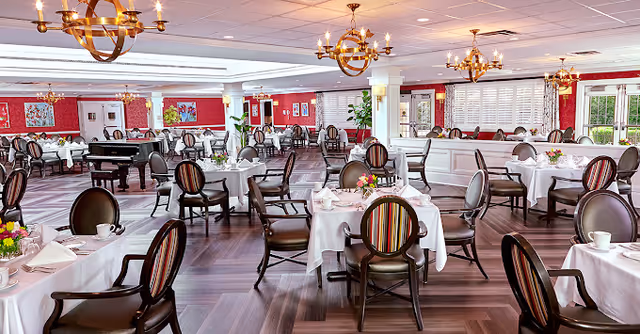 Spacious elegant dining room with round tables set with white tablecloths, upholstered chairs, and chandeliers.