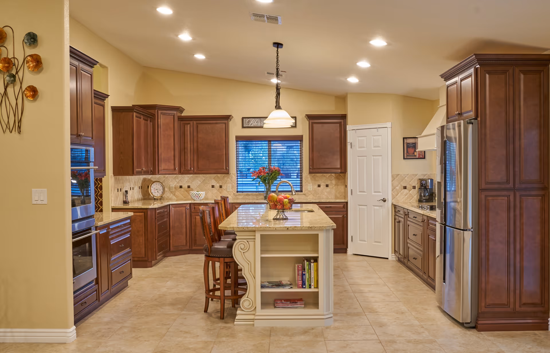 Well-lit spacious kitchen with a central island, wooden cabinets, stainless steel refrigerator, and bar stools.
