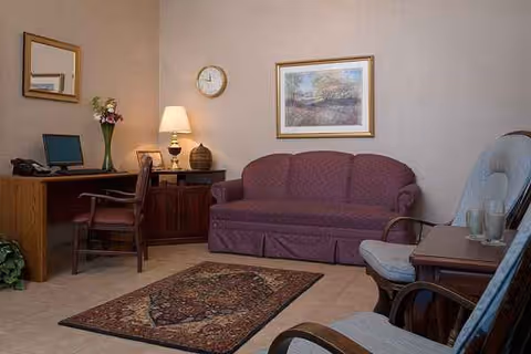Interior living room in Riverside Nursing & Rehab Center with sofa, desk, chairs, and artwork.
