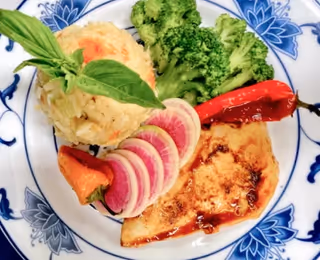 Plated meal with glazed grilled fish, mashed potatoes garnished with basil, sliced watermelon radish, broccoli, and a roasted pepper on a blue-and-white plate.