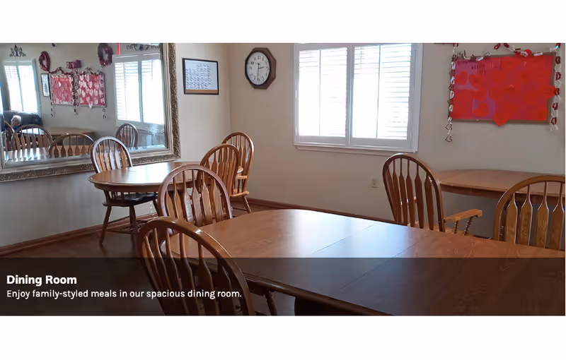 Spacious dining room with wooden tables and chairs, a large wall mirror, clock, and a bulletin board by a window.