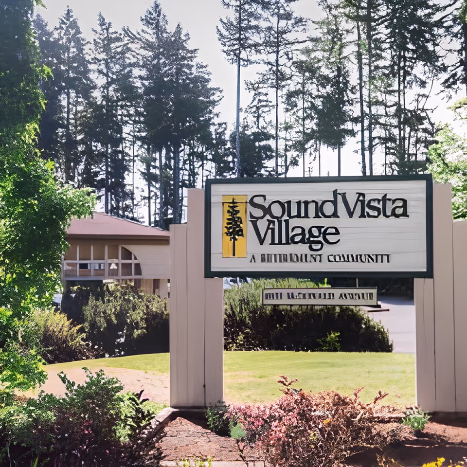 Entrance sign reading "Sound Vista Village" in front of landscaped grounds, trees, and a building.