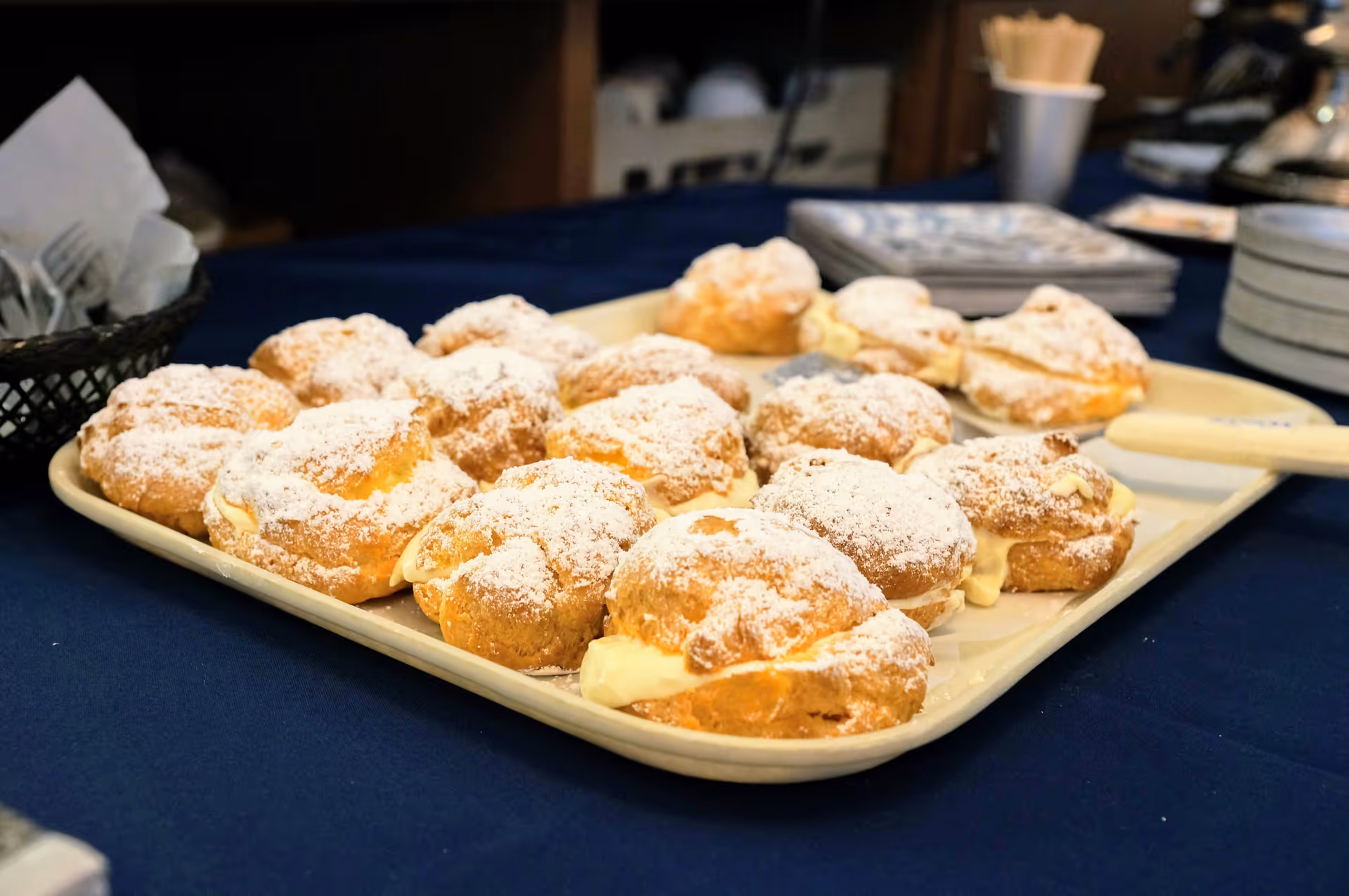 Tray of powdered sugar–topped cream puffs on a table with a blue tablecloth.