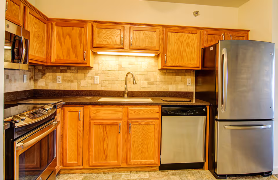 Well-lit kitchen with wooden cabinets, stainless steel appliances, a sink, and tiled backsplash.