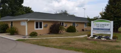Single-story beige senior living building with a landscaped sign on the lawn.