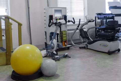Medical rehab gym with exercise bikes, elliptical, weights, and a large yellow exercise ball.