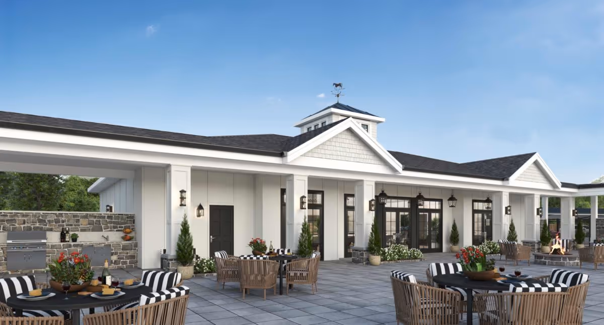 Outdoor patio with round tables, striped-cushion wicker chairs and potted plants in front of a white clubhouse-style building.