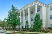 Front exterior of The Trace senior living building with tall white columns, three stories of windows, landscaping, and a driveway.