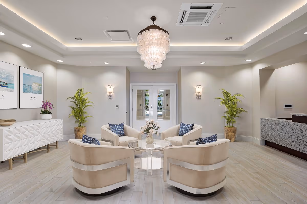 Bright modern lobby with four beige swivel chairs arranged around a glass coffee table beneath a chandelier.