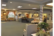 Spacious senior living facility common area with seating, a reception desk, plants, and decorative columns.
