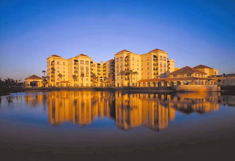 Multi-story Mediterranean-style building lit by golden sunset reflected in a calm lake.