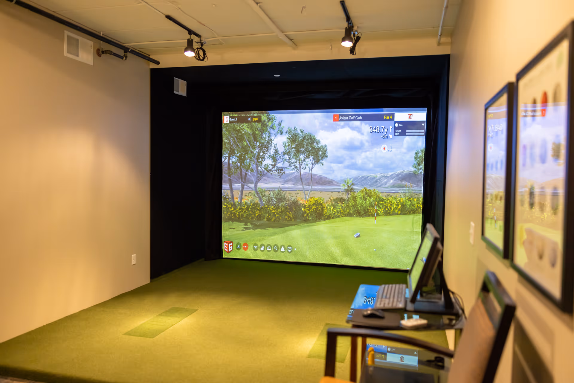 Indoor golf simulator room with a large projection screen showing a golf course and a putting green.
