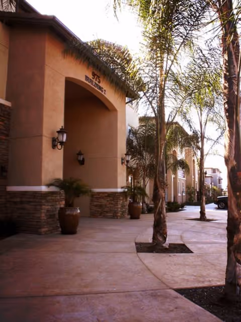 Exterior entrance of Woodland Village senior living, with palm trees, lights, and potted plants.