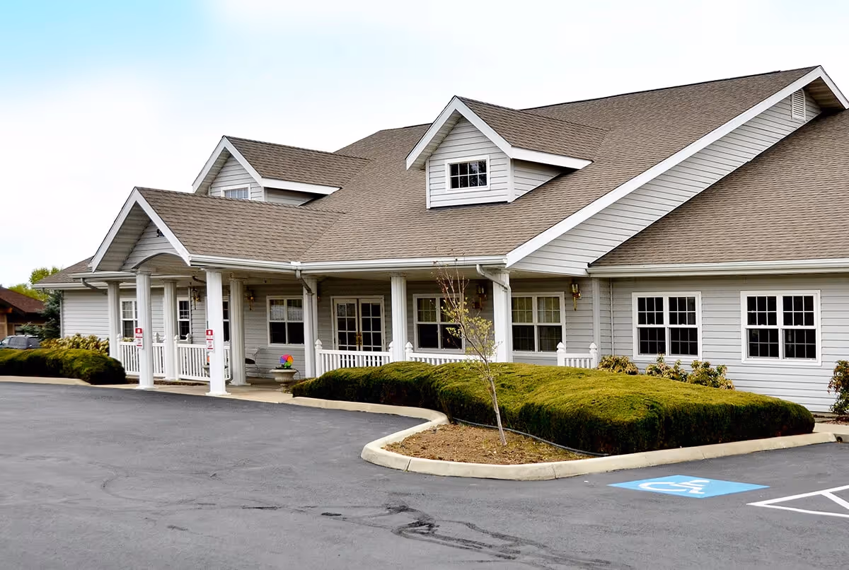 Front exterior of a single-story senior living facility with a covered entrance, white columns, and landscaped shrubs.