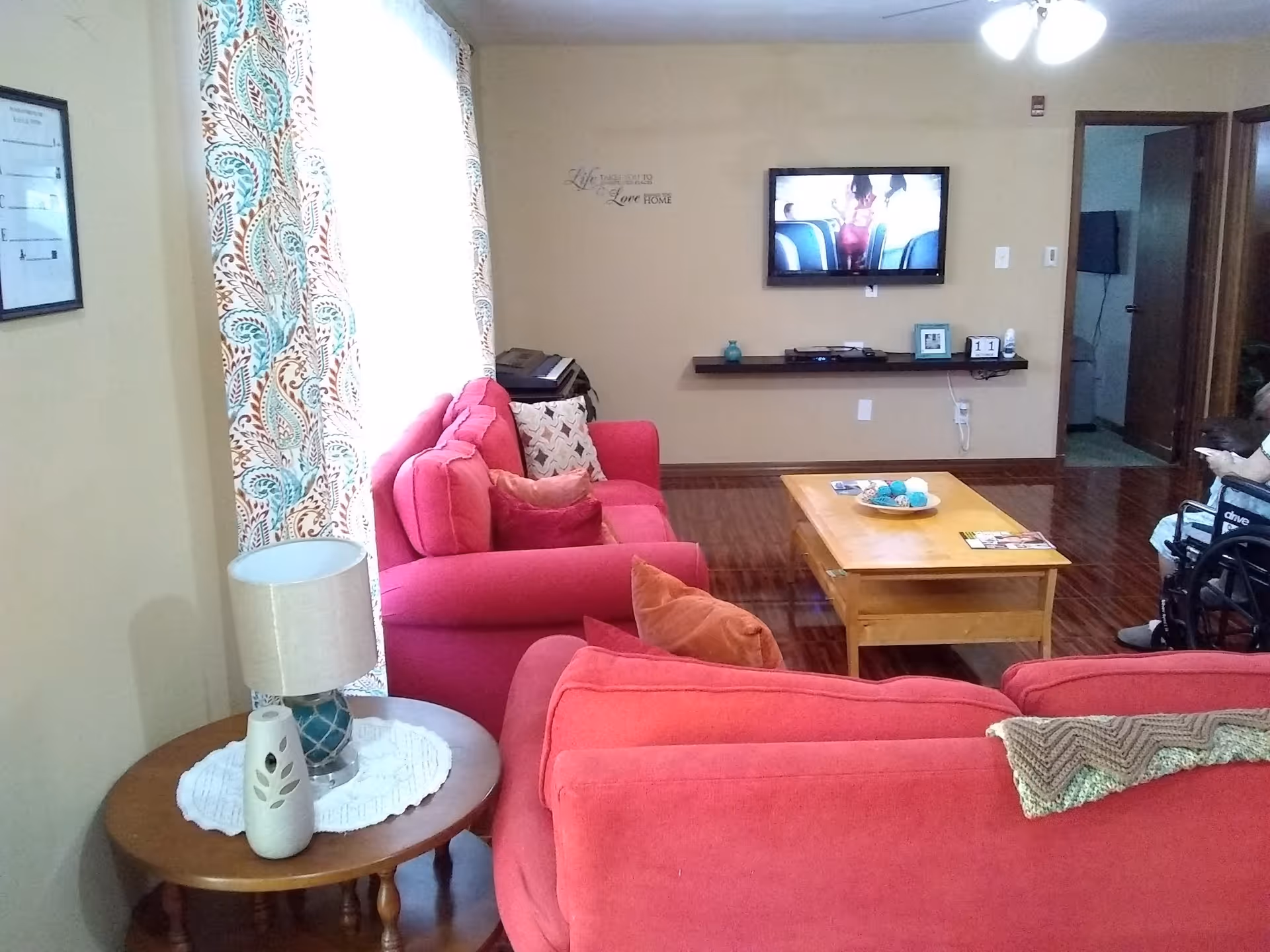 Cozy living room with red sofas facing a wall-mounted TV, a wooden coffee table, side table with a lamp, and wood floors.