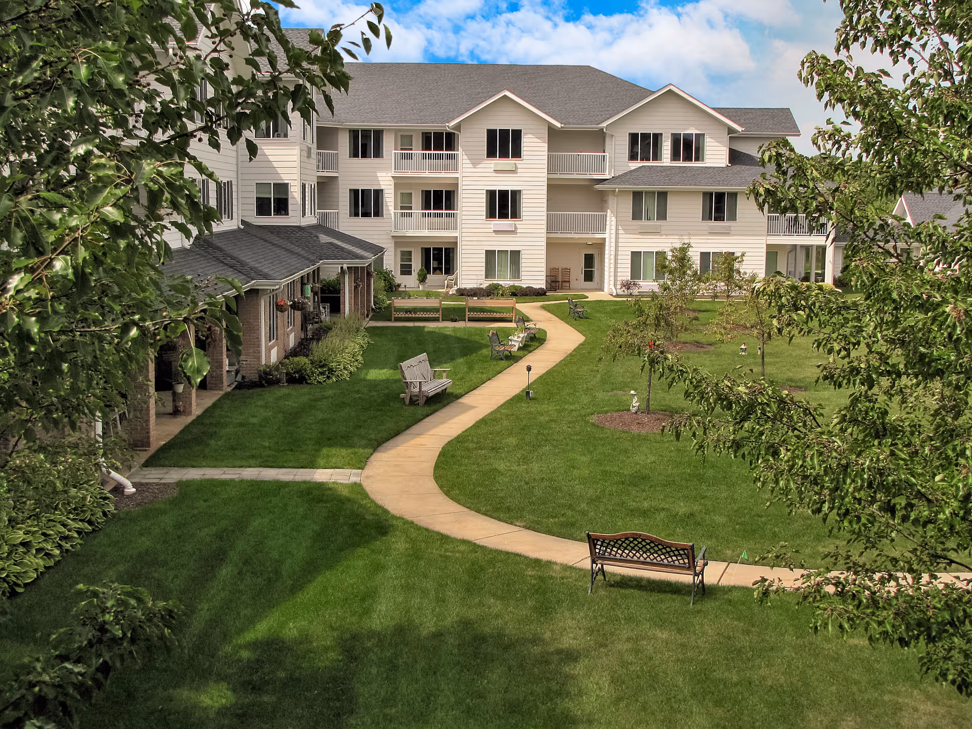 Landscaped courtyard with a winding walkway, benches, and a multi-story senior living building in the background.