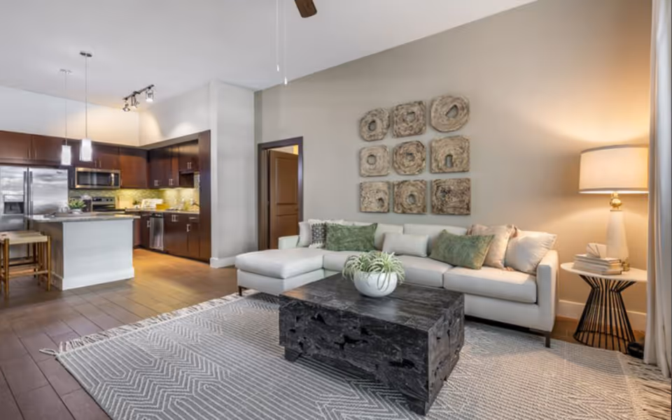 Open-concept living room with a sectional sofa, coffee table, decorative wall art and an adjacent kitchen with an island.