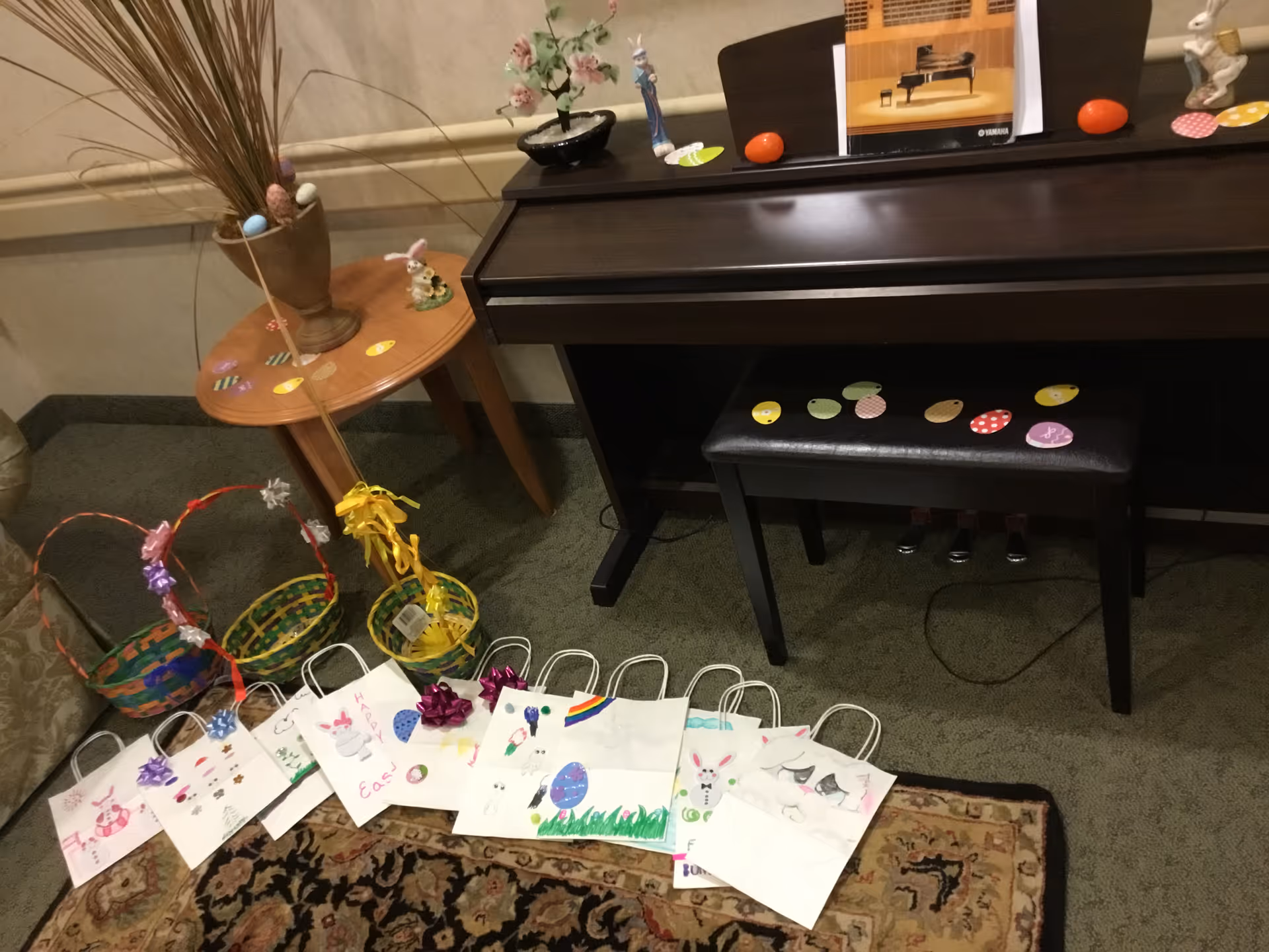 Digital piano and bench in a communal room surrounded by decorated Easter baskets, handmade gift bags, and a small side table with decorations.