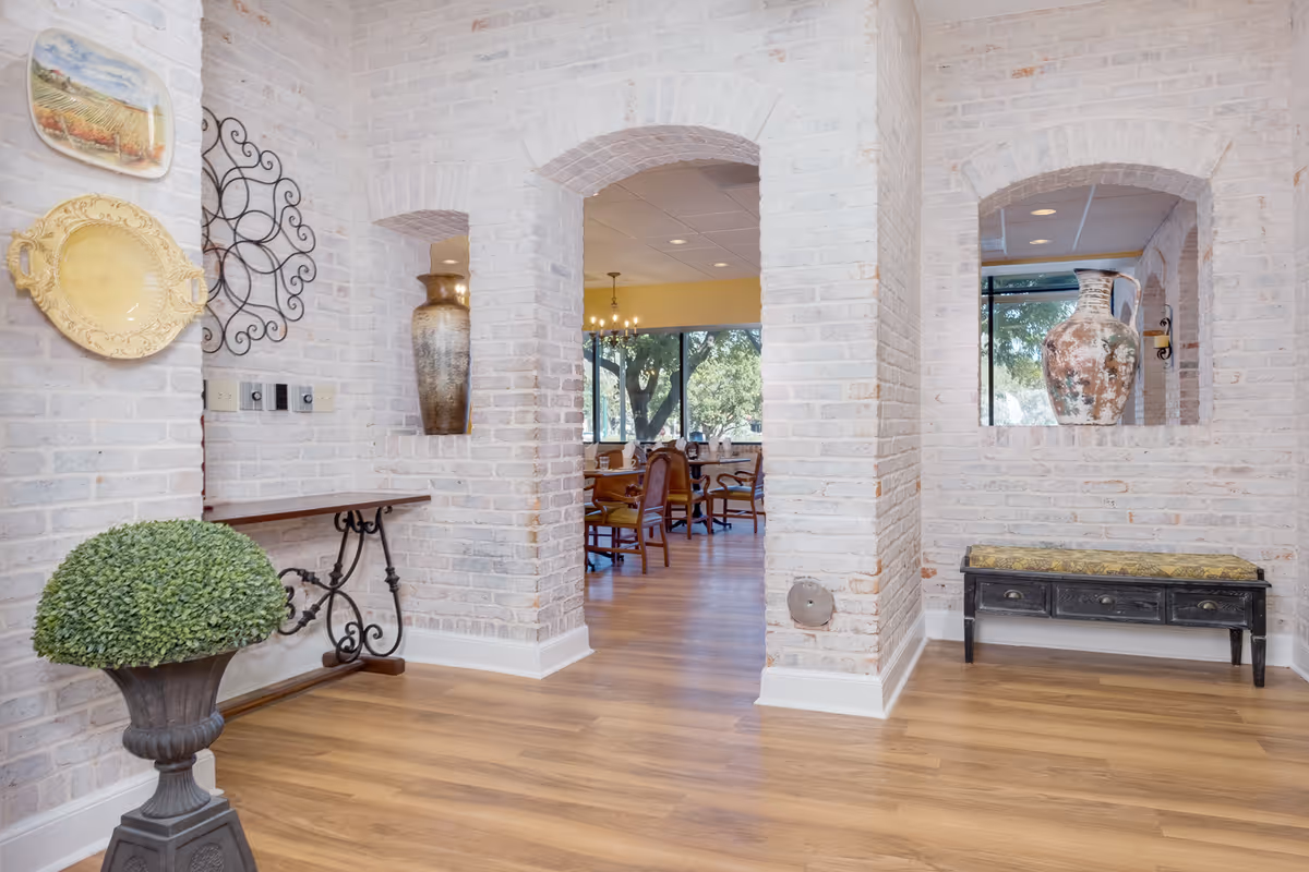 Bright brick-arched interior entry leading into a dining area with wooden floors, decorative vases, and seating visible through arches.