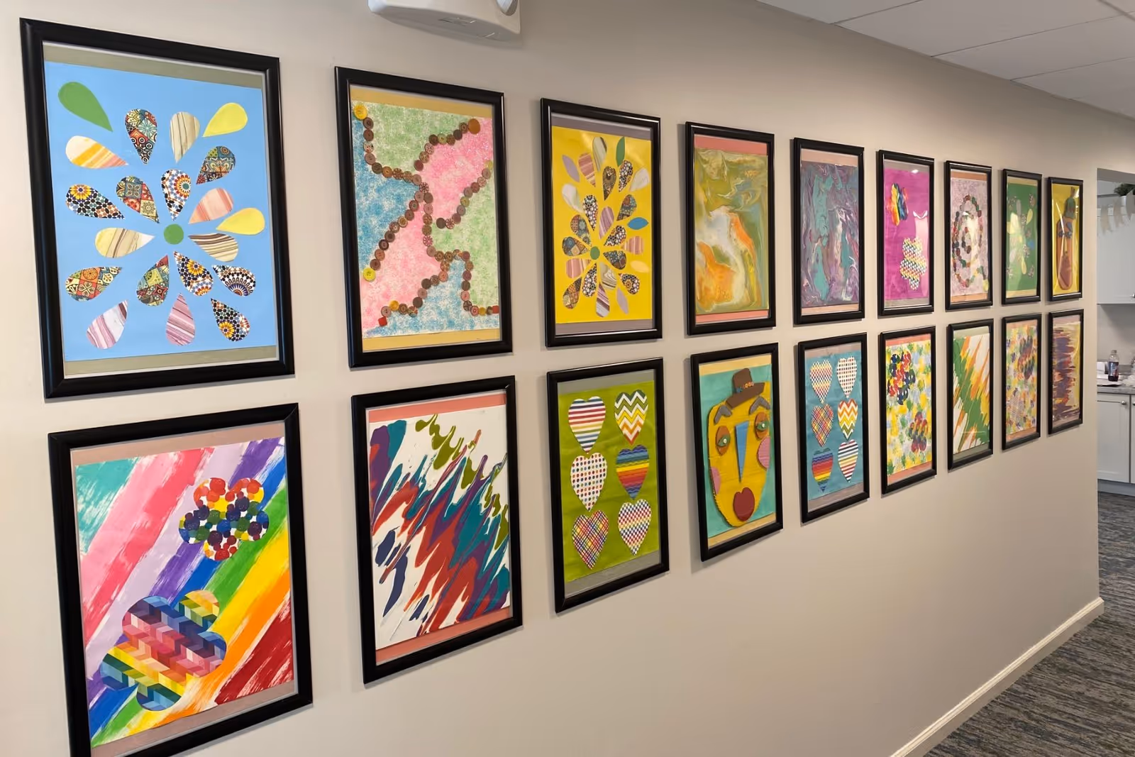 A hallway wall featuring two rows of framed colorful abstract and heart-themed artworks.