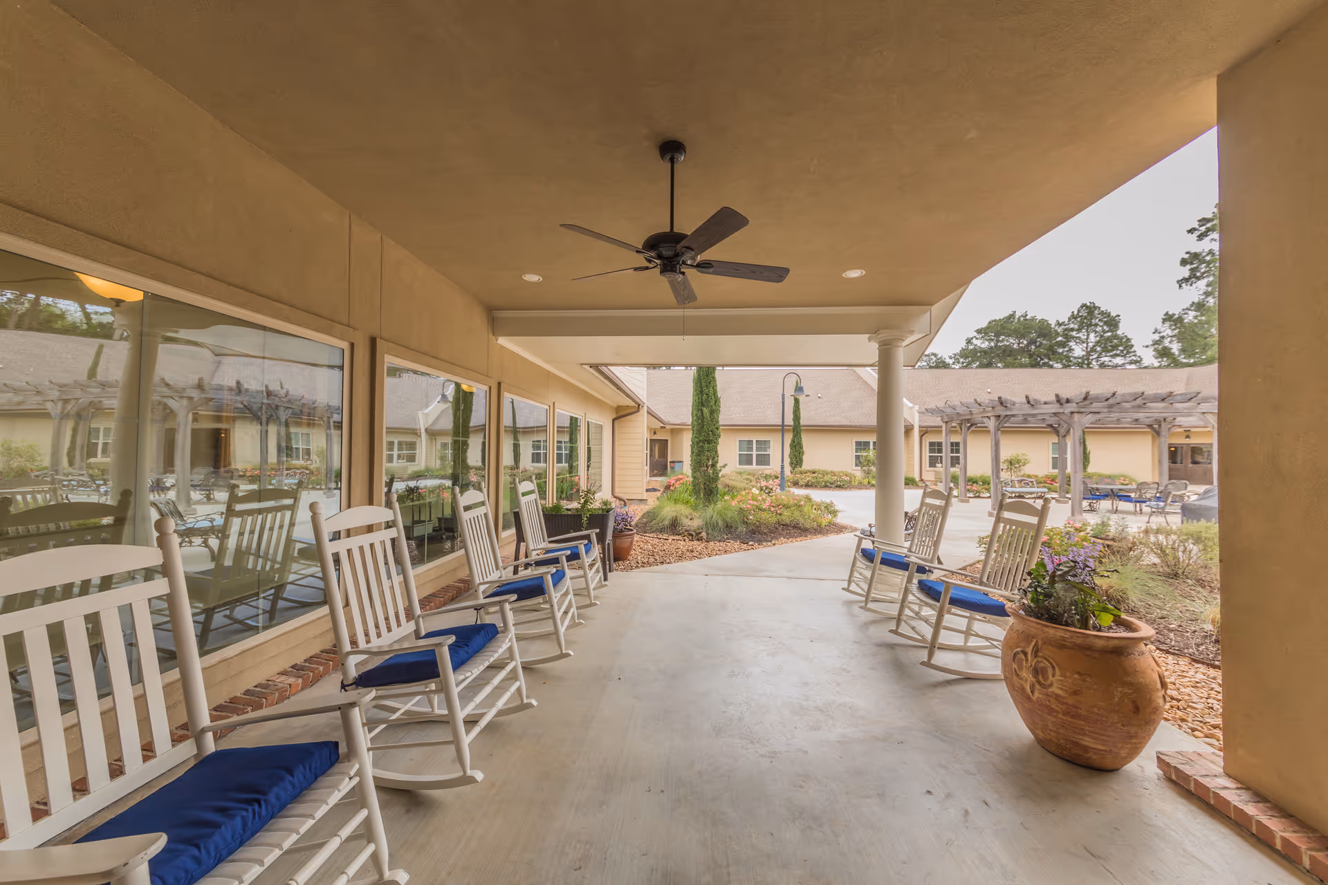 Covered porch with white rocking chairs with blue cushions facing a landscaped courtyard and pergola.