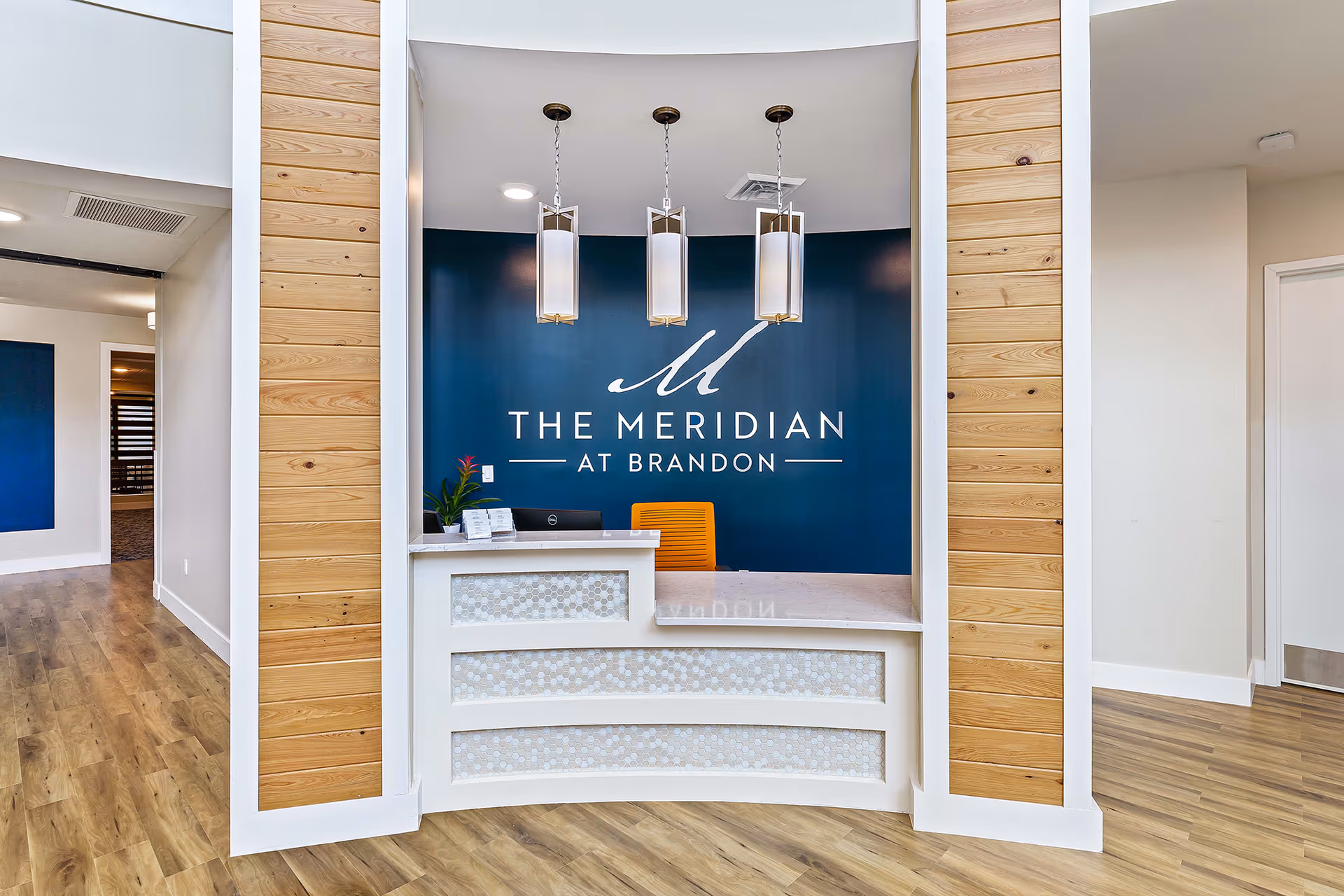 Reception desk area with three pendant lights and a blue wall sign reading 'The Meridian at Brandon'.