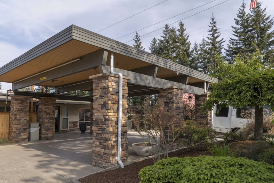 Exterior front entrance of Lynnwood Post Acute Rehabilitation Center with a stone-clad canopy, driveway, landscaping, and a white van.