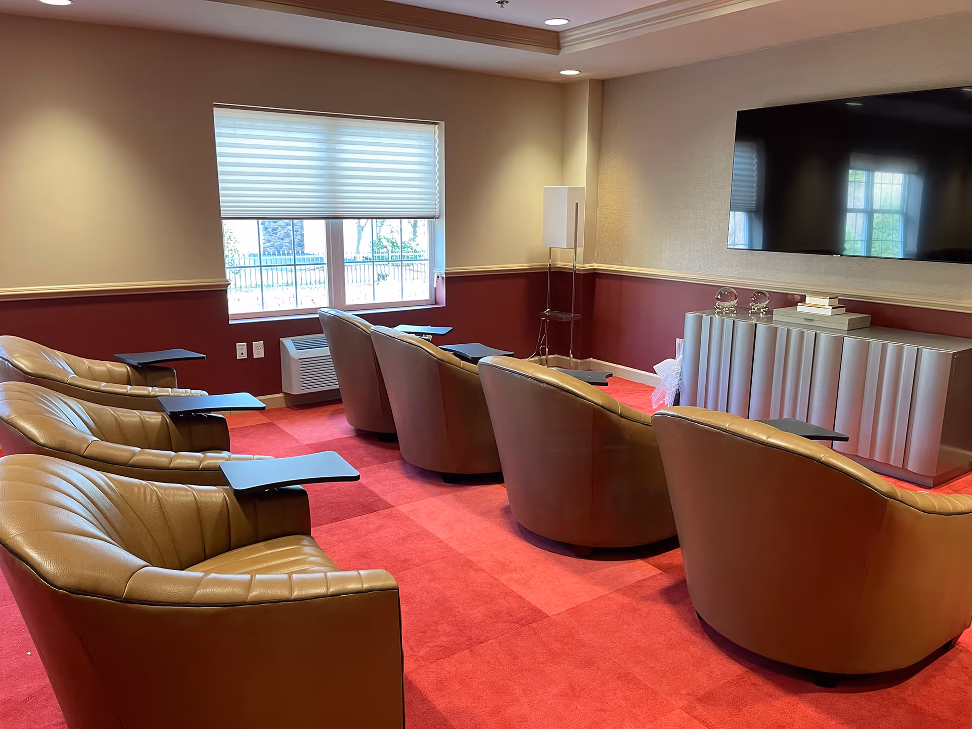 Cozy media room with leather armchairs arranged in rows facing a large wall-mounted TV and a console.
