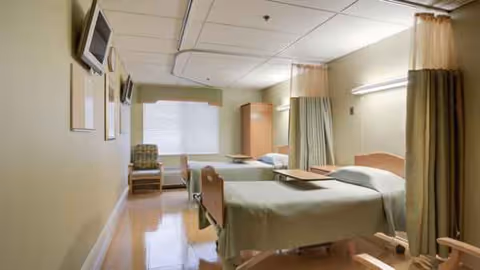 A patient room with two beds, privacy curtains, and chairs beside the window.