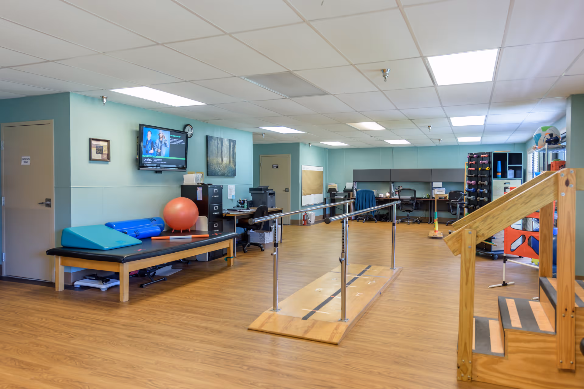 Interior therapy/exercise room with parallel bars, a treatment table, exercise balls, and wooden practice stairs.