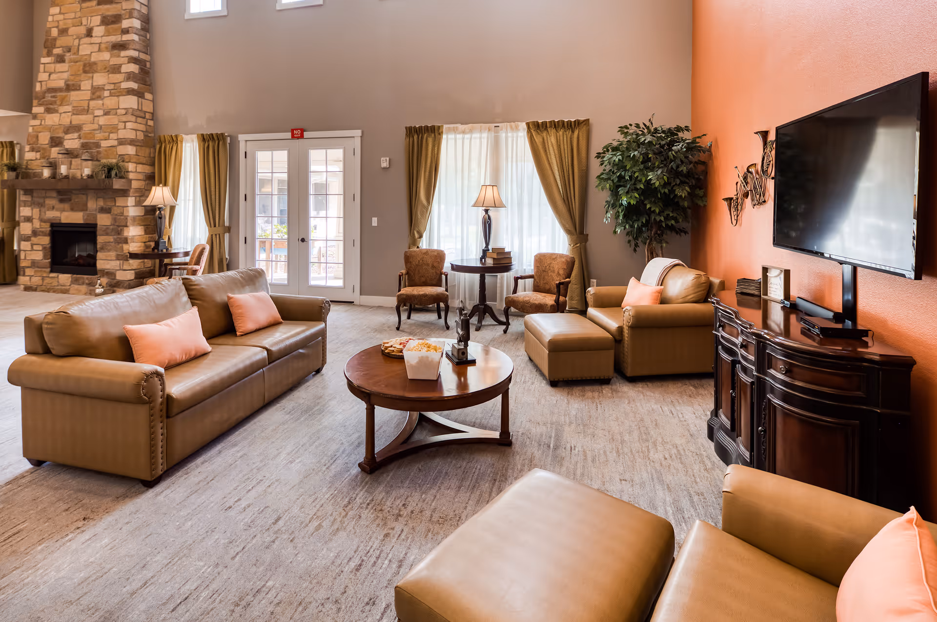 Bright furnished common living room with leather sofas, armchairs, a coffee table, fireplace, and wall-mounted TV.