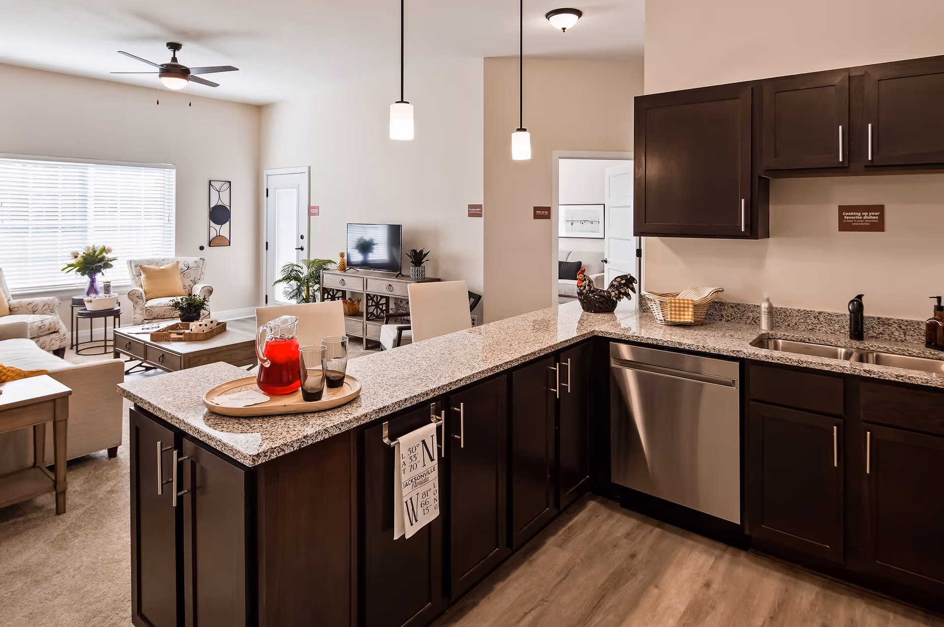 Open-concept kitchen with a granite island and dark cabinets opening onto a furnished living room.