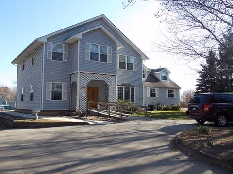 Two-story gray senior living building exterior with front entrance, driveway, and a parked vehicle.