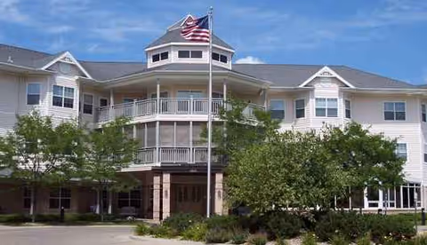 Two-story senior living facility with flagpole, balconies, and landscaped front entrance.