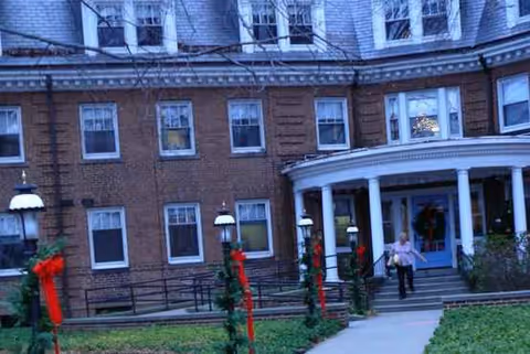 Brick senior living facility entrance with festive decorations and a person approaching the blue door.