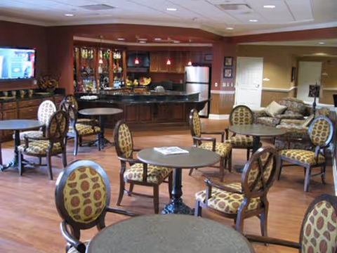 Spacious indoor living area with round tables, patterned chairs, and a kitchenette bar.