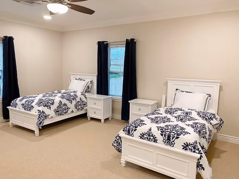 Two white twin beds with matching nightstands and navy patterned bedding in a bright bedroom.