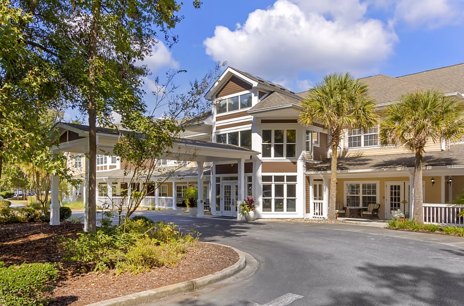 Front entrance of the Brookdale West Ashley senior living building with a covered porte-cochere, palm trees, and a landscaped driveway.